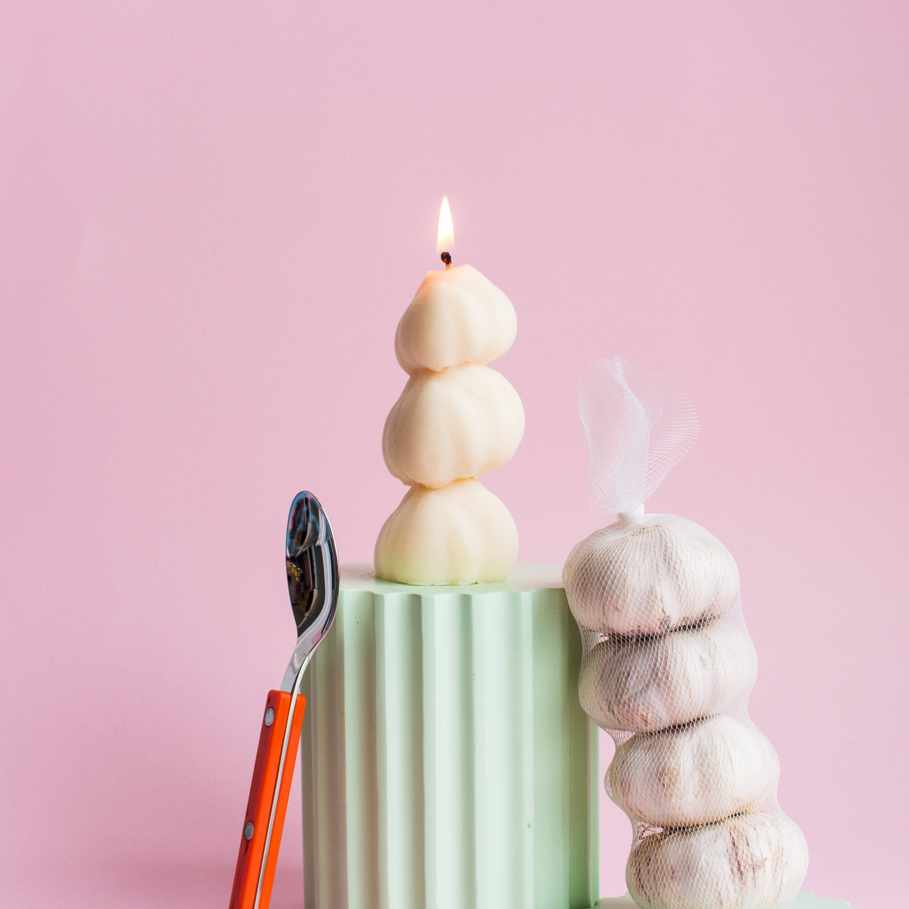 Stacked white candles on a green stand with a pink background
